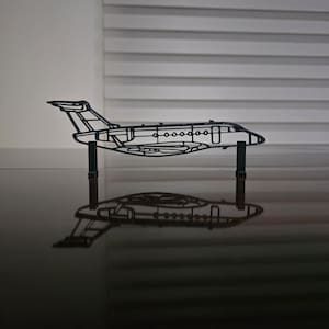 Può includere: Un modello di aereo in metallo nero, con un contorno dettagliato della struttura dell'aeromobile. Il modello è supportato da due piccoli supporti neri, creando un riflesso sulla superficie lucida. Il design mostra le ali, la fusoliera e i finestrini dell'aereo.