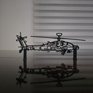 May include: A black metal helicopter model with detailed cutouts, standing upright on a dark surface. The model's design includes a main rotor, tail rotor, and fuselage, with a clear reflection below.