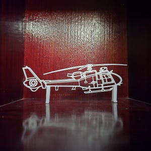 May include: A white, three-dimensional helicopter model with detailed outlines of the body, rotor, and tail. The model is displayed against a dark red background, with the helicopter's design clearly visible.