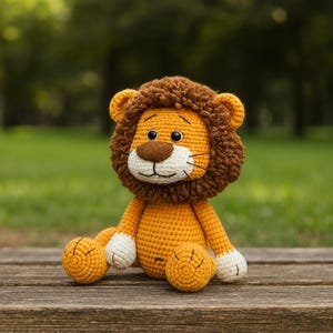 Peut inclure: Un jouet lion en crochet avec une crinière marron, un visage beige et un corps jaune. Le lion a des yeux noirs, un museau blanc et des pattes blanches. Il est assis sur une surface en bois avec un arrière-plan vert flou.