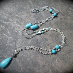 May include: A silver chain necklace with turquoise beads and a teardrop-shaped turquoise pendant.
