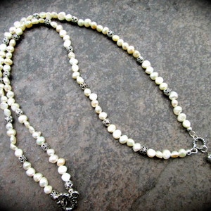 May include: A white pearl necklace with silver accents. The necklace is made of small, round pearls and has a silver clasp.