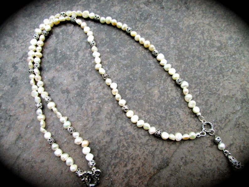 May include: A white pearl necklace with silver accents. The necklace is made of small, round pearls and has a silver clasp.