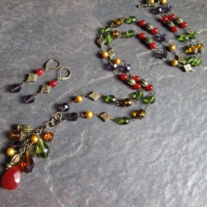 May include: A multi-strand necklace with red, green, gold, and purple beads. The necklace has a dangling charm with more beads. Matching earrings with red and purple beads.