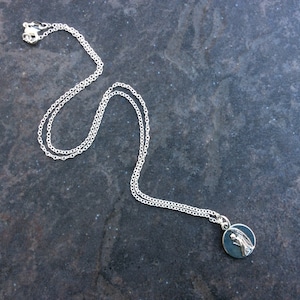 May include: A silver chain necklace with a small round pendant featuring a silver angel design.