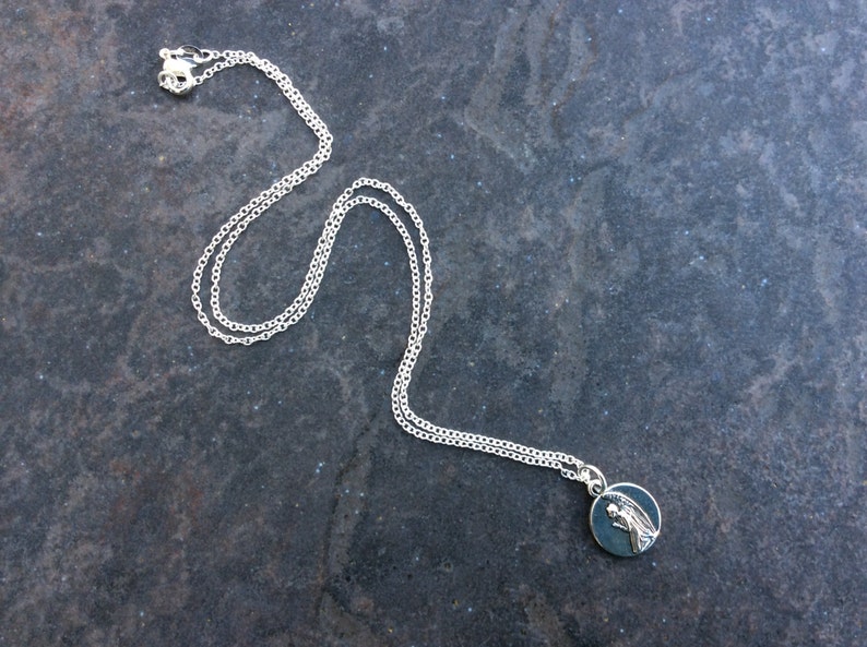 May include: A silver chain necklace with a small round pendant featuring a silver angel design.