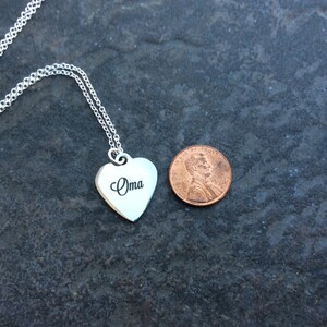 May include: A silver heart-shaped pendant necklace with the word " Oma" engraved on it. The pendant is about the size of a US penny.