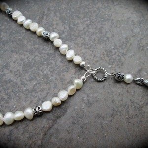 May include: A white pearl necklace with silver accents and a silver pendant. The pendant is shaped like a teardrop and has a decorative design.