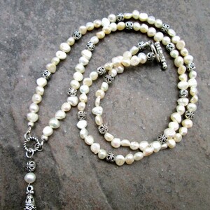 May include: A white pearl necklace with silver accents. The necklace has a drop pendant with a silver design.