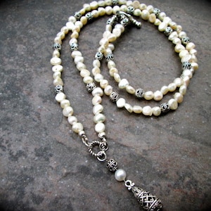 May include: A white pearl necklace with silver accents and a silver pendant. The necklace is layered and has a delicate design.