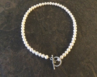 May include: A white pearl necklace with a silver toggle clasp.