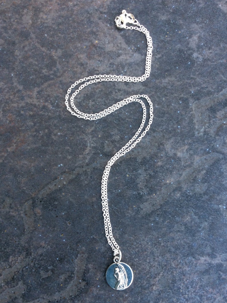 May include: A silver chain necklace with a round pendant featuring a silver image of a praying angel.