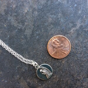 May include: A silver chain necklace with a small round pendant featuring a silver angel with wings. The pendant is about the size of a UK penny.