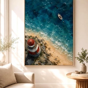 May include: A framed wall art print featuring an aerial view of a red and white lighthouse on a rocky coastline, with a small white boat floating in deep blue ocean water near a sandy beach, rendered in a textured, painterly style.