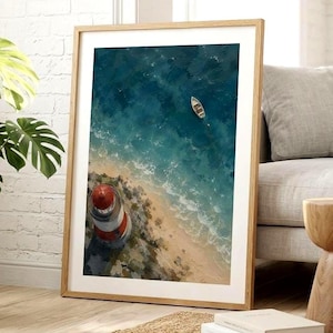 Könnte beinhalten: Ein gerahmter Kunstdruck mit einer Luftaufnahme eines rot-weißen Leuchtturms an einem Sandstrand mit türkisfarbenen Meereswellen und einem kleinen Boot im Wasser. Das Bild befindet sich in einem hellen Holzrahmen mit weißem Passepartout.