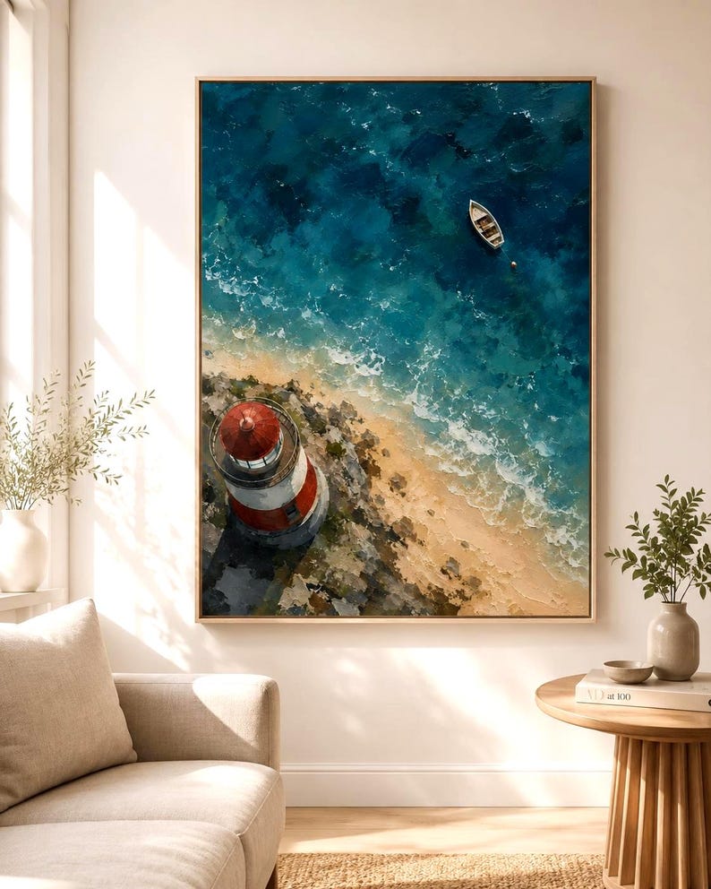 May include: A framed wall art print featuring an aerial view of a red and white lighthouse on a rocky coastline, with a small white boat floating in deep blue ocean water near a sandy beach, rendered in a textured, painterly style.