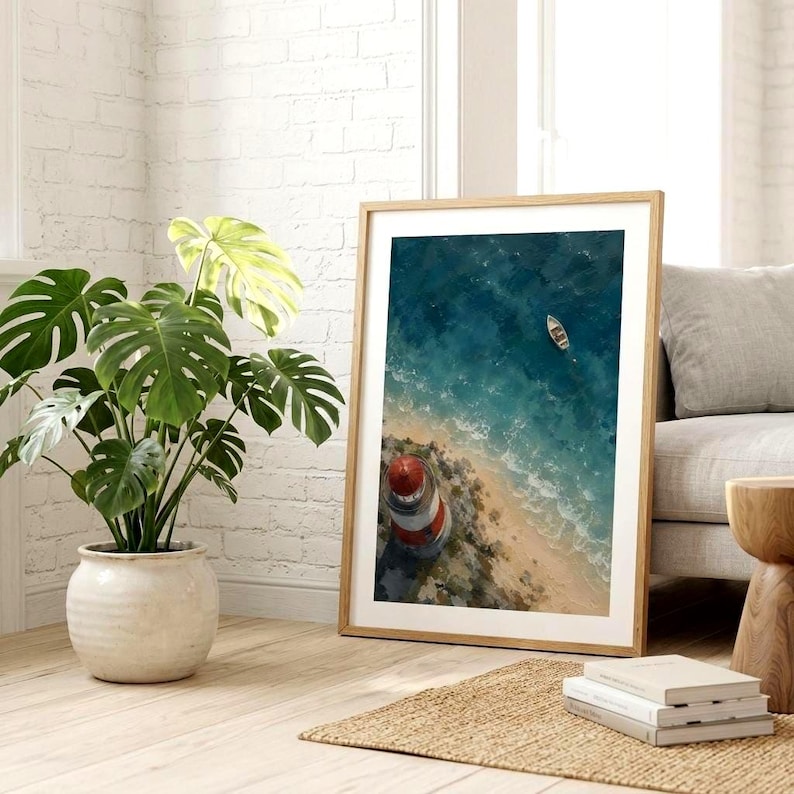 Könnte beinhalten: Ein gerahmter Kunstdruck mit einer Luftaufnahme eines rot-weißen Leuchtturms an einem Sandstrand mit türkisfarbenen Meereswellen und einem kleinen Boot im Wasser. Das Bild befindet sich in einem hellen Holzrahmen mit weißem Passepartout.