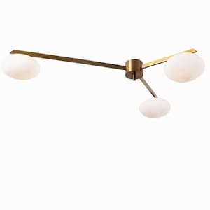 May include: A modern ceiling light fixture with three spherical white glass shades. The fixture has a brass finish with three arms extending from a central point. The arms are connected to the shades.