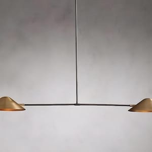 Op de afbeelding: Een moderne hanglamp met twee lampen met een minimalistisch ontwerp. De armatuur heeft twee conische, goudkleurige kappen die aan een zwarte horizontale balk zijn opgehangen. De lamp hangt aan een enkele zwarte staaf.