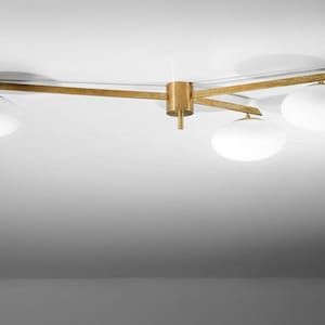 May include: A contemporary ceiling light fitting with a brass finish and three white globe shades. The fitting has a central cylindrical base and three arms extending outwards, each holding a globe. The light is mounted on a white ceiling.