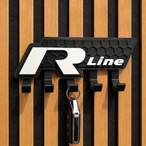 Könnte beinhalten: Schwarzer Schlüsselhalter mit weißem "R Line" Logo und vier Haken. Er ist an einer Holzwand mit vertikalen Streifen befestigt. Ein Schlüsselbund hängt an einem der Haken.
