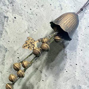 Peut inclure: Une cloche de style antique avec une finition bronze, ornée d'un motif floral et d'une chaîne de petites cloches ornées. Un accent de feuille décorative est attaché à la chaîne de la cloche. La cloche est probablement utilisée pour la décoration intérieure ou comme ornement unique.