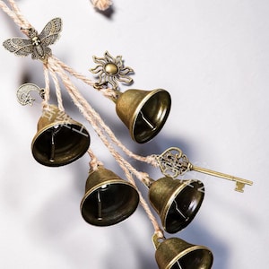 May include: A decorative wind chime with bronze-coloured bells, a butterfly, sun, moon and star, and key charms. The bells are suspended from natural twine.