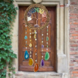 May include: A decorative wall hanging featuring a woven circular frame with a copper wire tree design. The tree is adorned with colorful gemstones, and strands of beads and agate slices hang below. The color palette includes blues, greens, yellows, oranges, and purples.