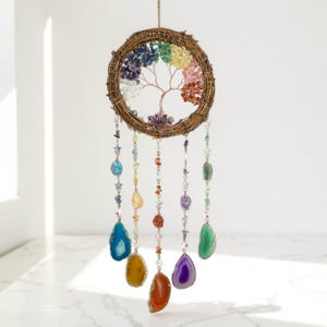 Puede incluir: Un atrapasoles artesanal con forma de árbol de la vida con un marco circular tejido. El árbol presenta un diseño de alambre de cobre con hojas de piedras preciosas de colores. Cadenas de piedras preciosas de varios colores cuelgan debajo.