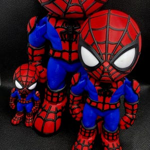 May include: Three Spider-Man figurines of varying sizes, each featuring a red and blue suit with black web patterns and large white eyes. The figures are standing upright, showcasing a consistent design with a prominent black spider emblem on the chest.
