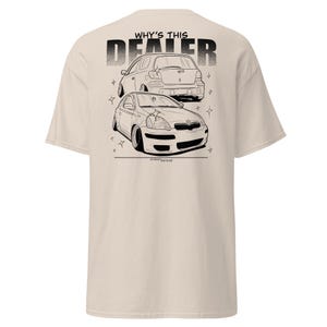 Puede incluir: Camiseta beige con un gráfico en blanco y negro de dos coches y el texto "WHY'S THIS DEALER" encima. Los coches están estilizados con suspensión rebajada. Prenda de vestir informal.