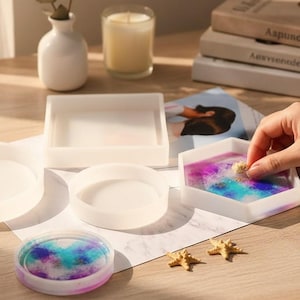 May include: A selection of white silicone moulds in different shapes, including round, square, and hexagonal. One mould contains a colourful, swirled resin design. Decorative starfish and a lit candle are also present.
