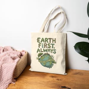 May include: Cream-colored tote bag with the text "EARTH FIRST, ALWAYS" in green and brown lettering. The bag features a globe graphic with the words "SUSTAIN, PROTECT, THRIVE" on a banner. A bicycle graphic is also included.