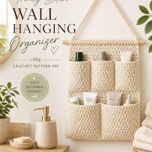 Könnte beinhalten: Ein cremefarbener Wand-Organizer aus Häkelarbeit mit fünf Taschen, der an einem Holzstab hängt. Der Text lautet Trinity Stitch WALL HANGING Organizer, CROCHET PATTERN PDF, EASY BEGINNER FRIENDLY, 5 POCKET DESIGN, 100% COTTON YARN, TEXTURED & MODERN, BEAUTIFUL & PRACTICAL.