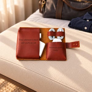 May include: A brown leather tech organizer with a snap closure, featuring two interior pockets and two elastic loops. The left pocket is engraved with "Every adventure is better with you by my side" and the right pocket with "Forever your person, Emma."