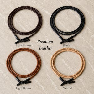 May include: Four braided leather cords arranged in a grid, labeled Premium Leather. The cords come in dark brown, black, light brown, and natural colors, each featuring black metal clasps at the ends for securing items like glasses or charms.