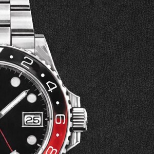 K&ouml;nnte beinhalten: Nahaufnahme einer Edelstahl-Armbanduhr mit schwarzem Zifferblatt und rot-schwarzer L&uuml;nette. Das Zifferblatt zeigt das Datum an, und die Zeiger sind sichtbar. Das Armband der Uhr ist ebenfalls aus Edelstahl.