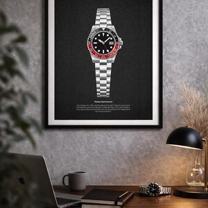 K&ouml;nnte beinhalten: Gerahmter Druck einer Edelstahl-Armbanduhr mit schwarzem Zifferblatt und rot-schwarzer L&uuml;nette. Die Uhr ist auf einem schwarzen Hintergrund zentriert. Der Druck enth&auml;lt den Text "Timeless Dual-time Icon".