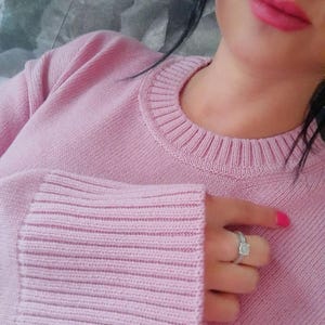Può includere: Un maglione in maglia a maniche lunghe color rosa chiaro con scollo rotondo a coste e ampi polsini a coste. Il maglione è realizzato in un filato morbido e testurizzato con un motivo a maglia uniforme su tutto il capo, per un aspetto pulito.