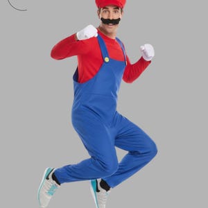 May include: A person in a Mario costume jumps in the air. The costume includes a red cap with a white "M", a red long-sleeve shirt, blue overalls, white gloves, and a black mustache. The person is wearing gray and blue sneakers.