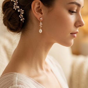 Peut inclure: Une boucle d'oreille dorée composée d'un petit cristal transparent, d'une tige métallique en forme de branche ornée de minuscules pierres claires et d'une perle blanche en forme de goutte. Un peigne à cheveux assorti est également porté.