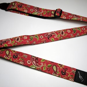 Pu&ograve; includere: Tracolla per chitarra rossa con motivo paisley verde, marrone e bianco. La tracolla ha estremit&agrave; in pelle nera e una fibbia di regolazione in plastica nera. La tracolla &egrave; progettata per essere indossata sulla spalla.