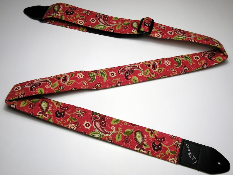 Pu&ograve; includere: Tracolla per chitarra rossa con motivo paisley verde, marrone e bianco. La tracolla ha estremit&agrave; in pelle nera e una fibbia di regolazione in plastica nera. La tracolla &egrave; progettata per essere indossata sulla spalla.