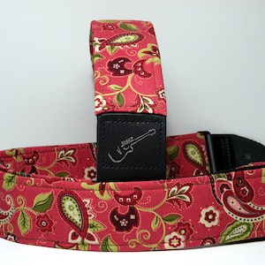 Pu&ograve; includere: Una tracolla per chitarra rossa con motivo paisley e dettagli verdi e bianchi. La tracolla ha un'estremit&agrave; in pelle nera con la scritta "JAMZ" e una silhouette di chitarra. Per chitarre elettriche.