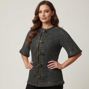 May include: A short-sleeved chainmail shirt with leather accents and buckle closures. The shirt is a dark gray color and features a round neckline and short sleeves. The leather detailing runs down the front of the shirt, with several buckles for closure. This medieval-inspired garment is suitable for cosplay or historical reenactments.