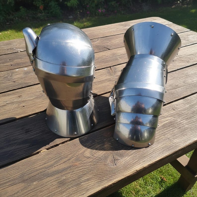 May include: Two shiny, silver metal gauntlets, likely for historical reenactment or display, rest on a wooden surface. The gauntlets are highly reflective, with articulated fingers and wrist protection, showcasing a medieval or Renaissance aesthetic.