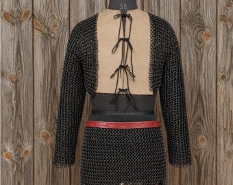 May include: A full suit of chainmail armor displayed on a mannequin. The armor is black with a tan backing and a red belt. The mannequin is set against a wooden background.