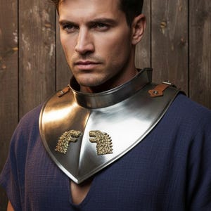 May include: A silver-colored gorget with two gold-colored lion emblems. The neck armor is secured with brown leather straps and rivets. The person is wearing a blue shirt, and the background is a wooden wall.