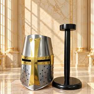 May include: A silver-colored metal great helm featuring a prominent gold-colored cross overlay on the front, multiple ventilation holes along the lower section, and a black wooden display stand with a circular base and a vertical support post.