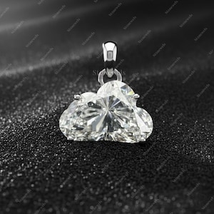 Può includere: Un pendente a forma di cuore con diamante e montatura in argento. Il pendente è trasparente e sfaccettato, riflettendo la luce. Lo sfondo è una superficie scura e strutturata, che esalta la brillantezza del pendente. È un gioiello.